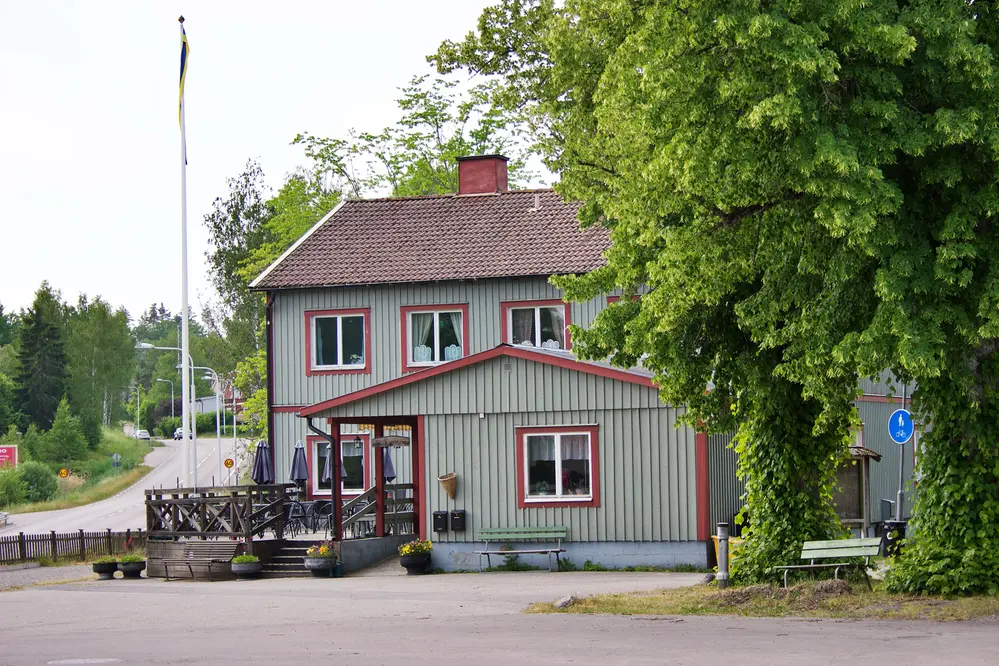 Ett grå/grönt trähus med storveranda och röda lister
